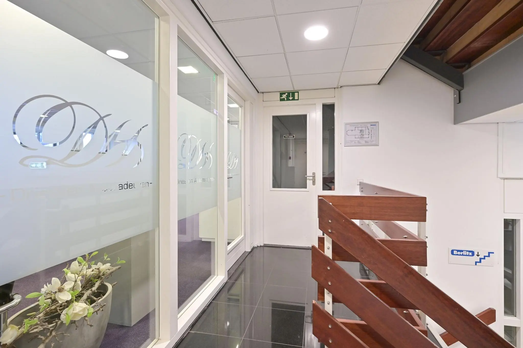 Binnenhal van een kantoorpand aan de Koninginnegracht met houten trap, glazen deuren met bedrijfslogo en bewegwijzering van Berlitz.