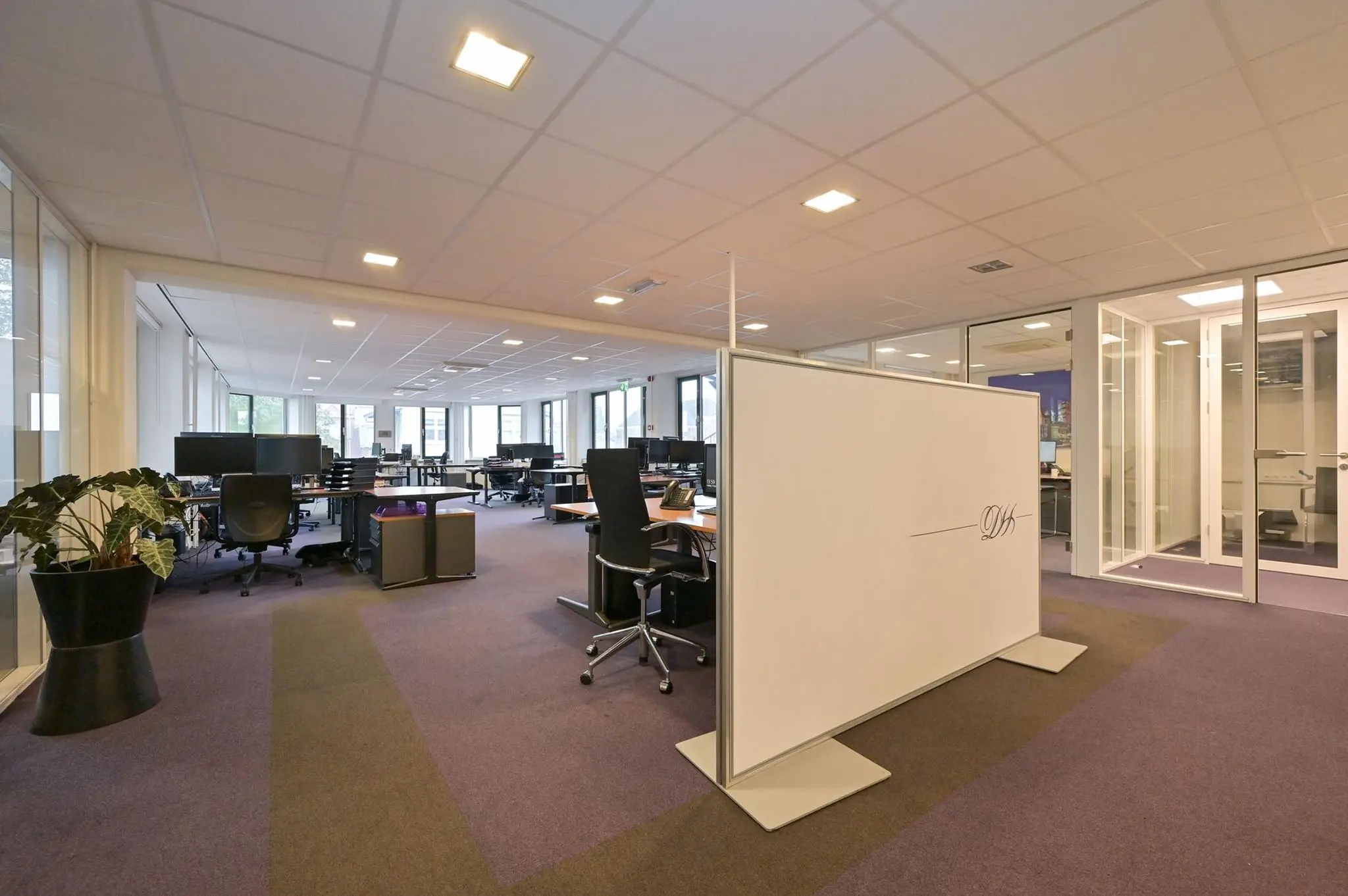 Modern en ruim kantoorinterieur aan de Koninginnegracht met werkplekken, glazen wanden en paarse vloerbedekking.