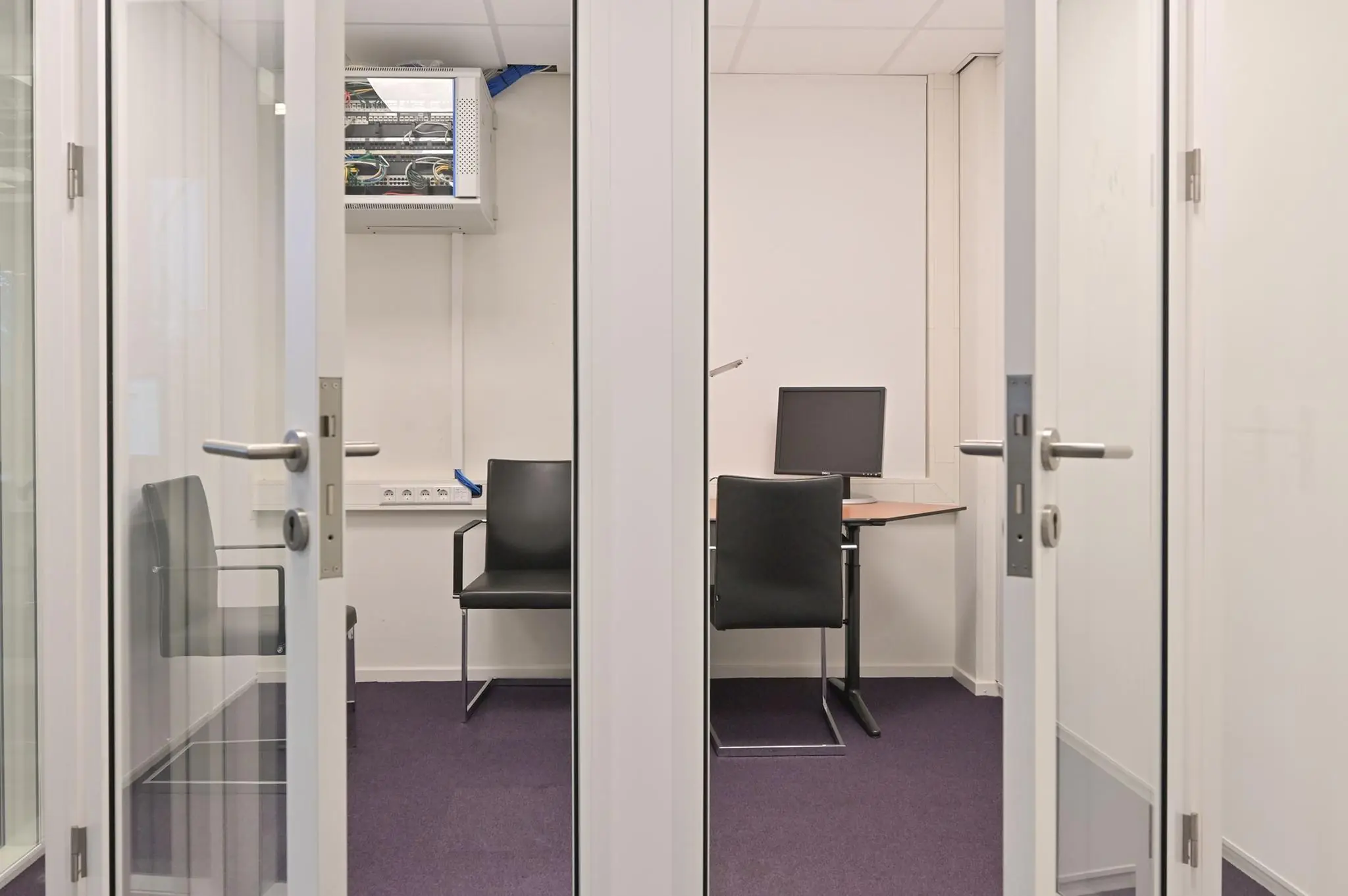 Kleine vergaderruimte aan de Koninginnegracht met twee stoelen, een bureau en een computer.