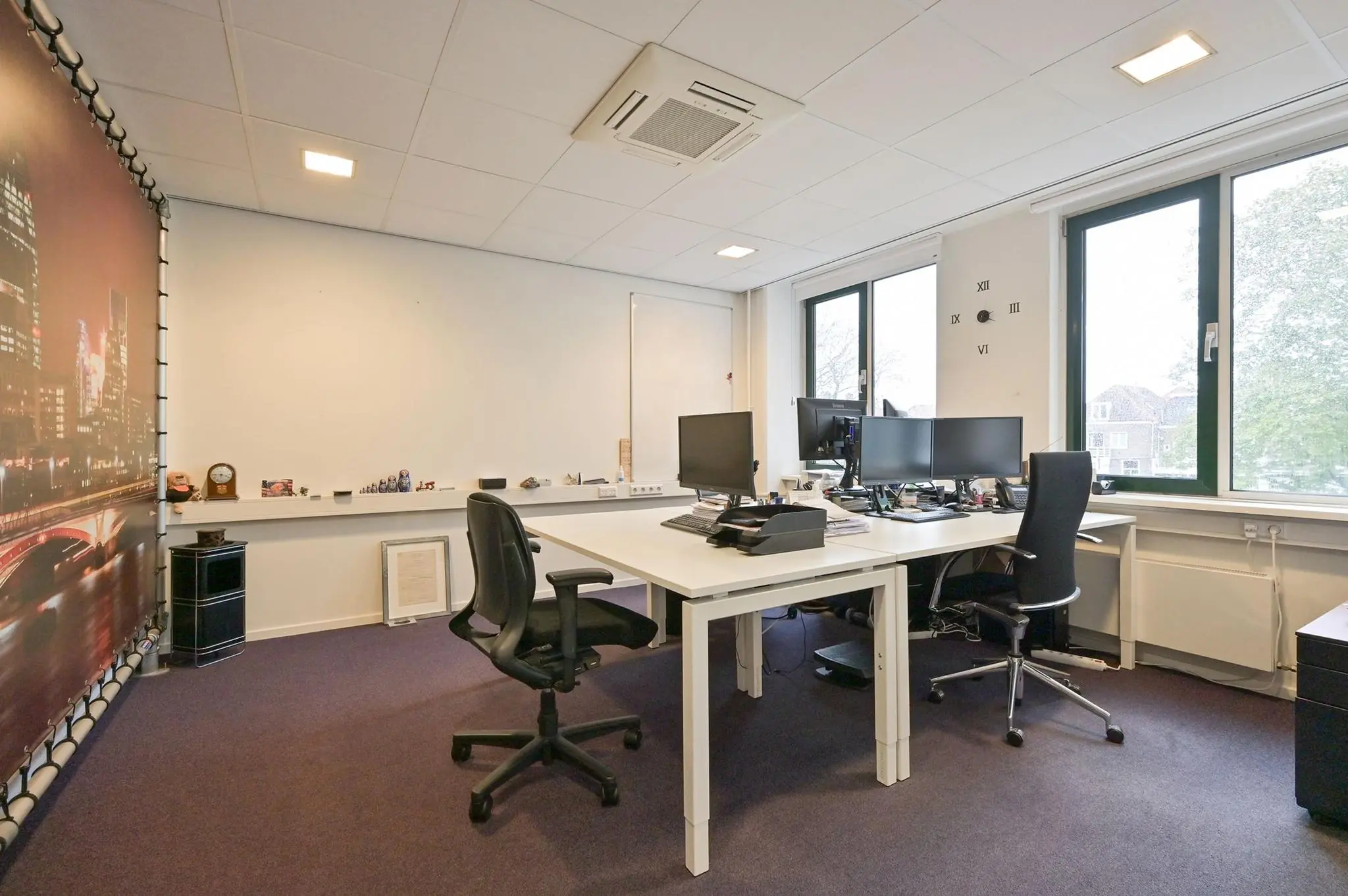 Modern kantoor met twee bureaus, meerdere computerschermen en grote ramen aan de Koninginnegracht.