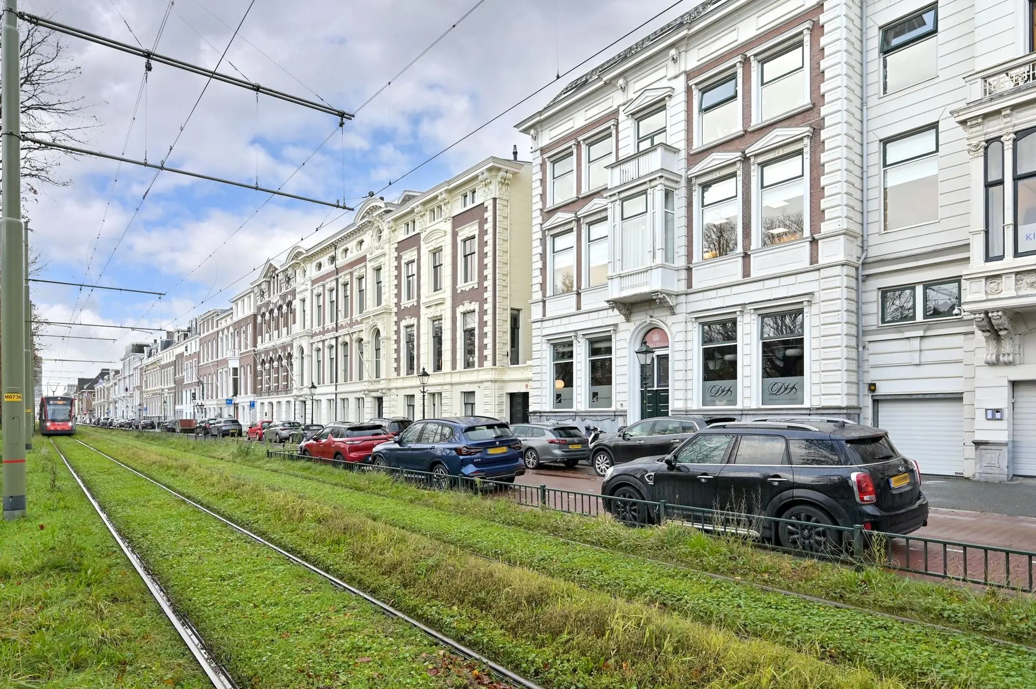 Straatbeeld van de Koninginnegracht in Den Haag met een tram, geparkeerde auto's en monumentale panden.