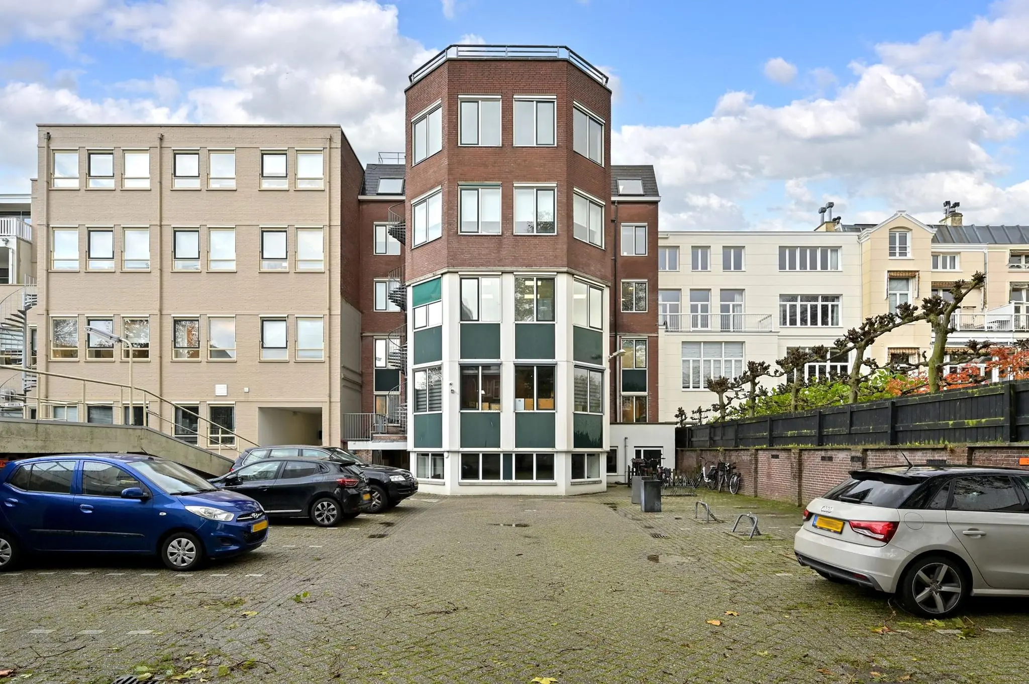 Achterzijde van een kantoorgebouw aan de Koninginnegracht met geparkeerde auto's en fietsenrekken op een binnenplaats.