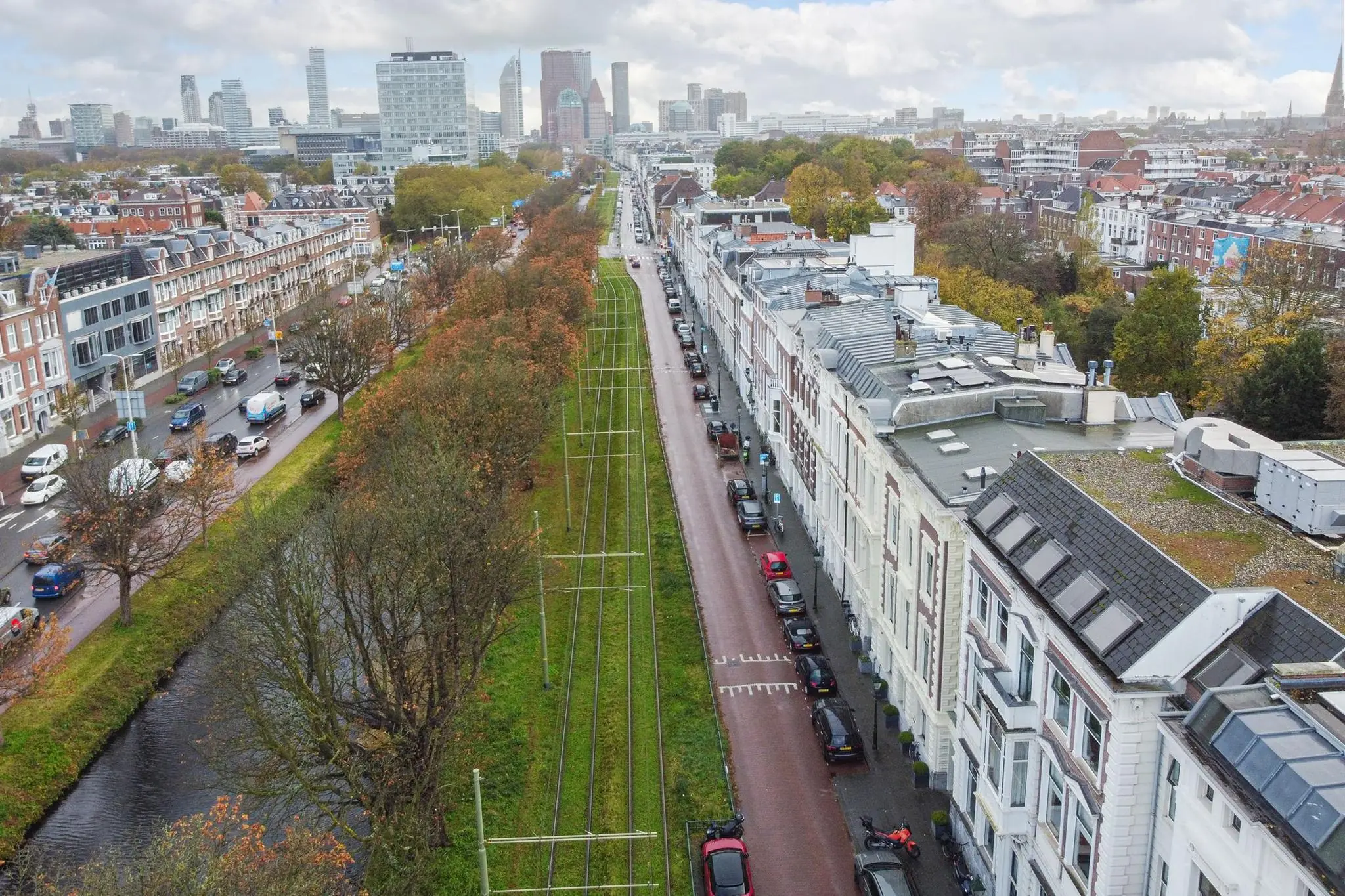 Luchtfoto van de Koninginnegracht in Den Haag met trambaan, rijwoningen en uitzicht op de skyline.