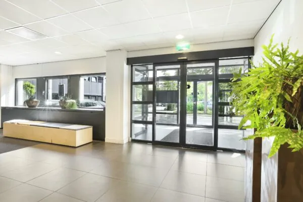 Lichte en moderne entreehal aan de Winthontlaan met automatische glazen deuren, planten en een zitbank.