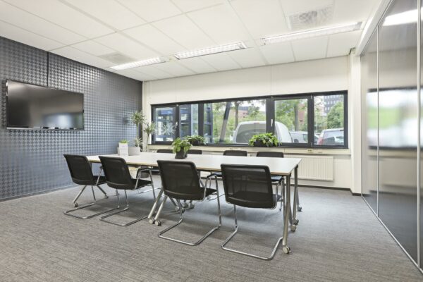 Moderne vergaderruimte aan de Winthontlaan met een lange tafel, zwarte stoelen, een flatscreen en grote ramen met uitzicht op geparkeerde auto's.
