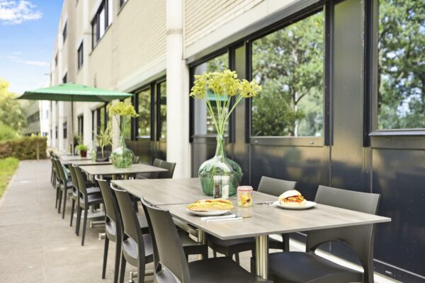 Terras met moderne tafels en stoelen aan de Winthontlaan, gedekt met eten en grote groene vazen met bloemen.