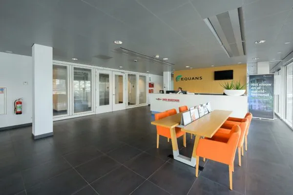 Moderne ontvangsthal van het Equans-kantoor aan de Willingestraat, met een balie, zitgedeelte en promotiebanner.