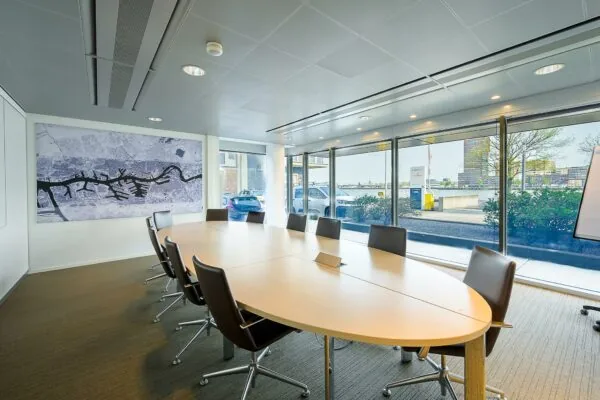 Vergaderruimte aan de Willingestraat met ovale tafel, lederen stoelen, kaart van de stad aan de muur en uitzicht op het water en moderne gebouwen.