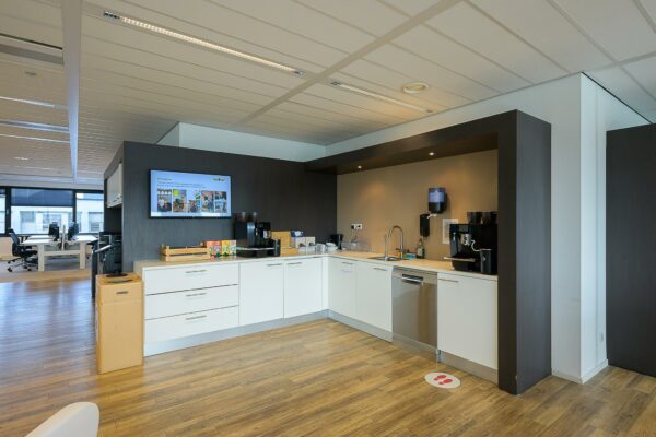 Moderne kantoorkeuken aan de Willingestraat met koffiezetapparaten, vaatwasser en een zithoek op de achtergrond.