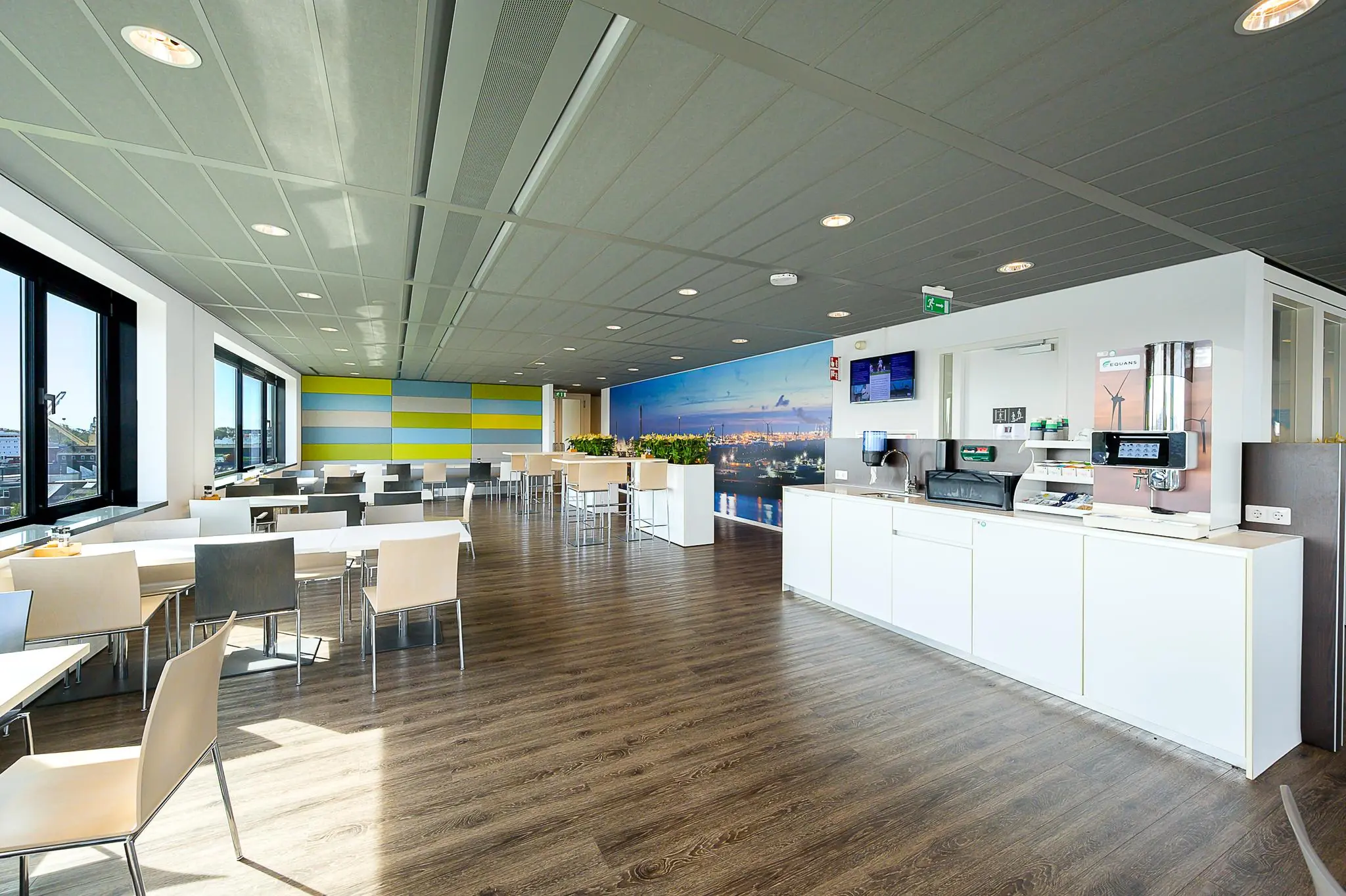 Modern bedrijfsrestaurant aan de Willingestraat met kleurrijke wandpanelen, panoramisch havenfotobehang en zelfbedieningskoffiehoek.