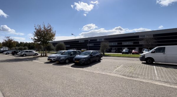 Parkeerplaats met auto's voor een modern zwart bedrijfspand aan de Bergveste op een zonnige dag.
