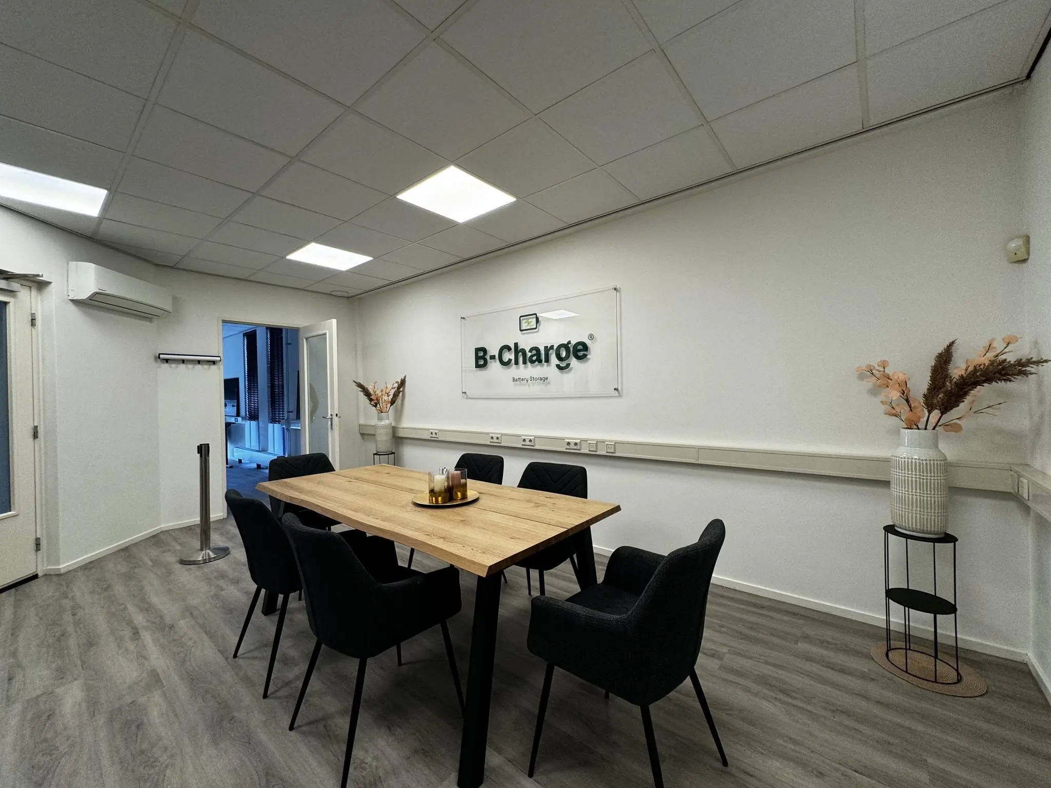 Vergaderruimte van B-Charge met een houten tafel, zes zwarte stoelen en een moderne, minimalistische inrichting.