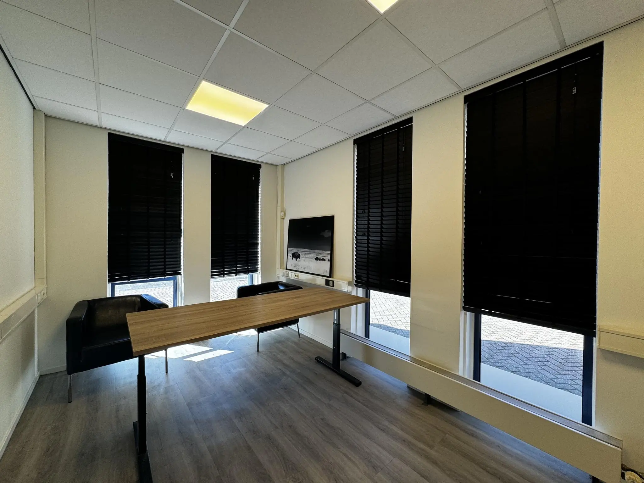 Moderne vergaderruimte bij Bergveste met houten tafel, zwarte stoelen, zwarte lamellen en een flatscreen aan de muur.