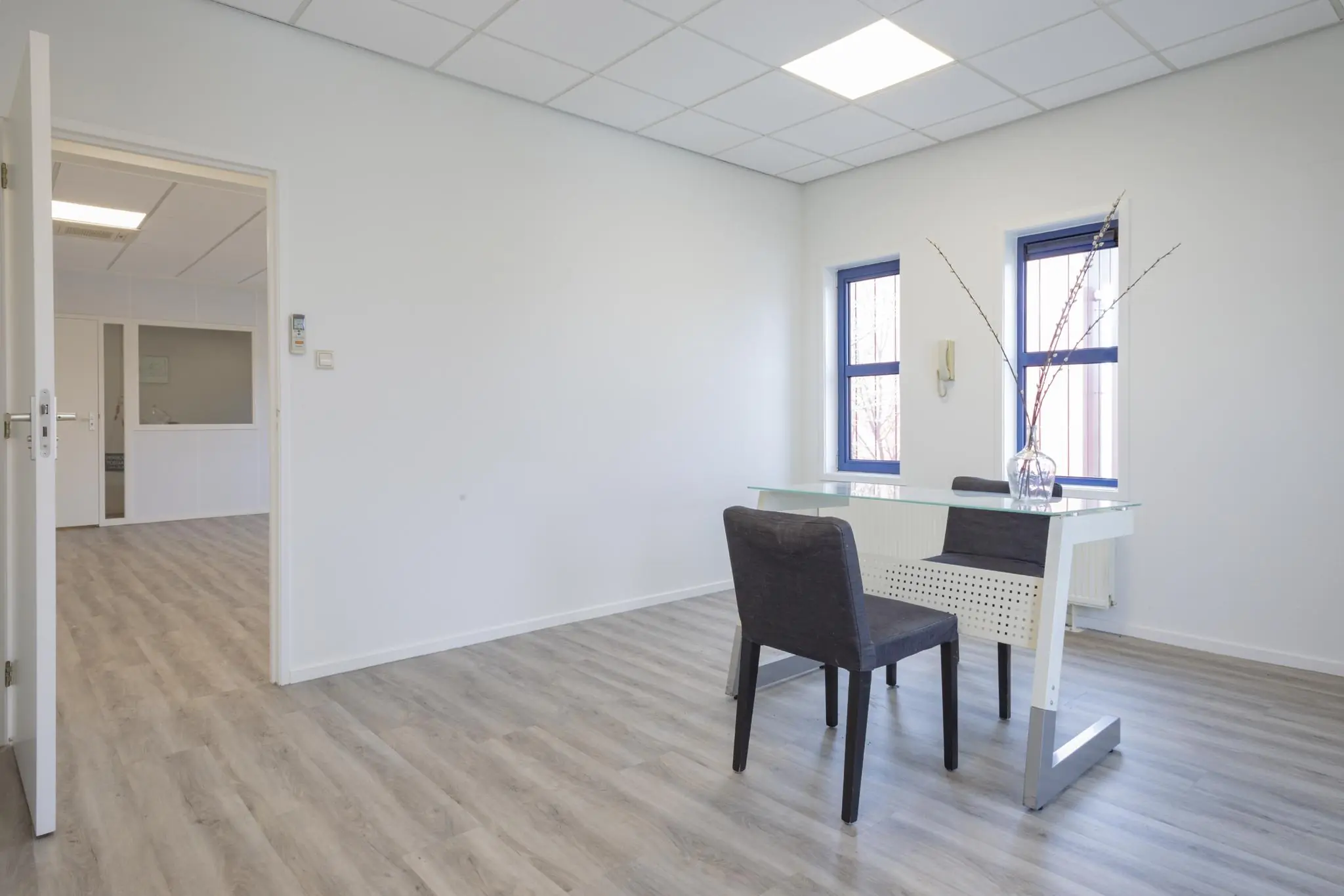 Licht en modern kantoor met een glazen bureau, twee stoelen en grote ramen in Bergveste.