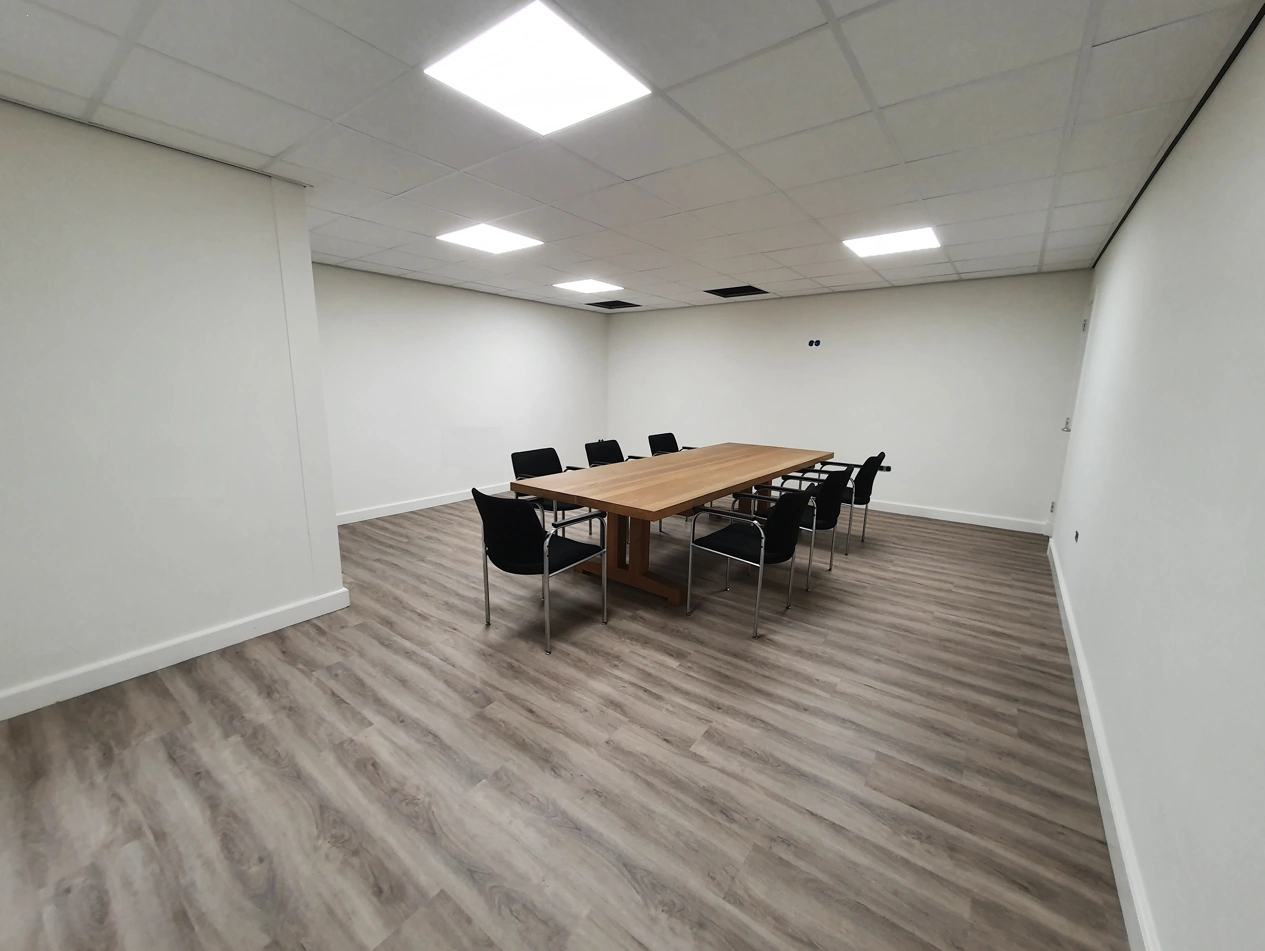 Vergaderruimte met een houten tafel, acht zwarte stoelen en een lichte vloer in Bergveste.
