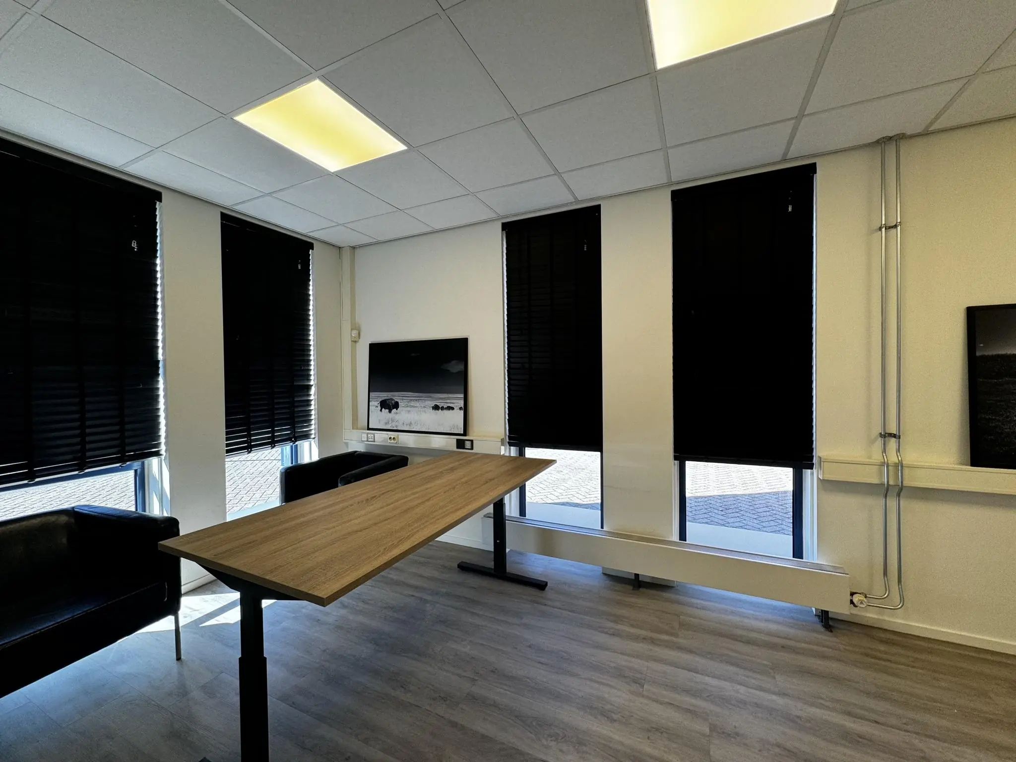 Vergaderruimte in Bergveste met houten tafel, leren stoelen, zwarte jaloezieën en wandkunst.