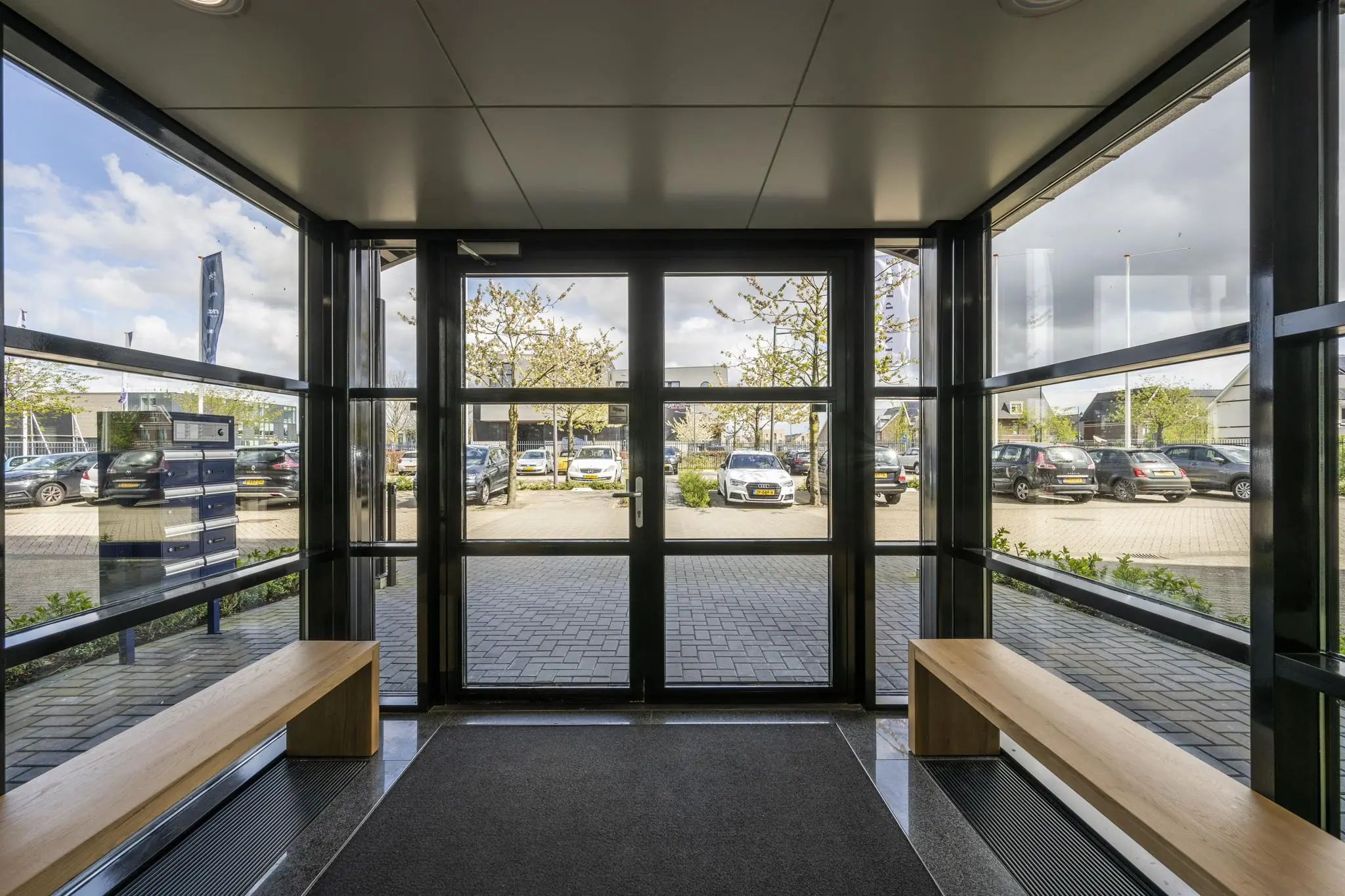 Ingang met glazen deuren en ramen aan de Singaporestraat, met uitzicht op een parkeerterrein en bloeiende bomen.