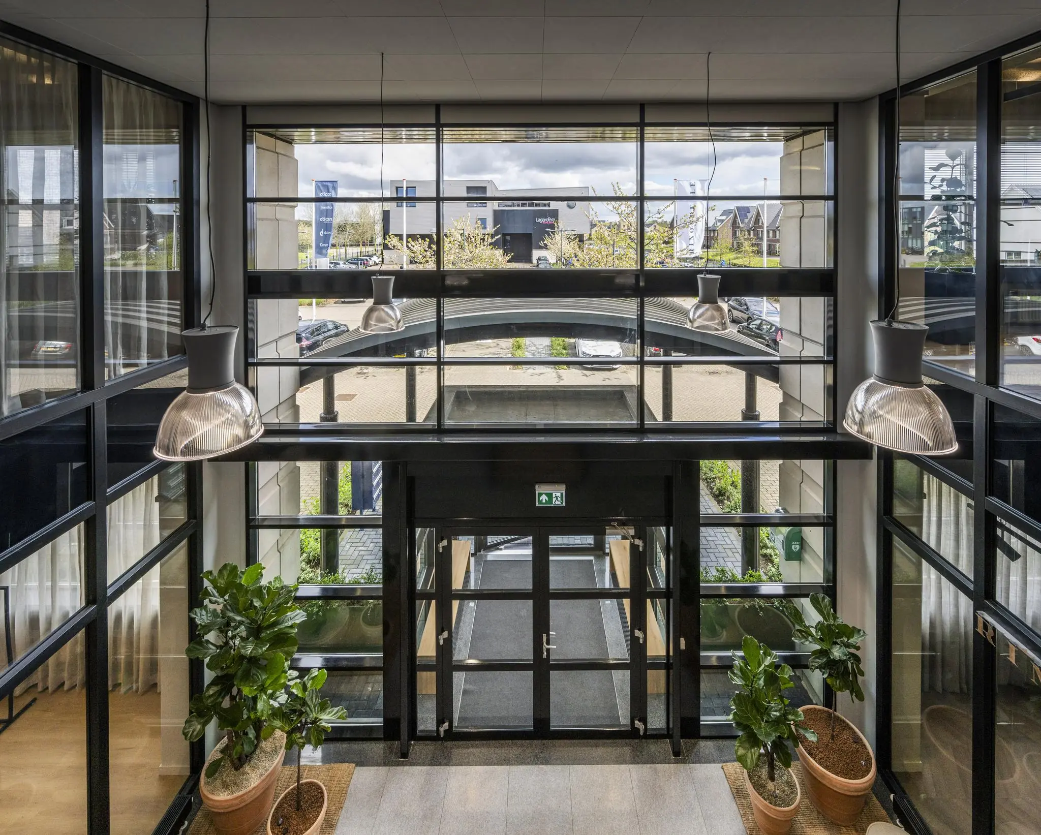 Inkomhal met glazen gevel, grote hanglampen, kamerplanten en uitzicht op bedrijventerrein aan de Singaporestraat.