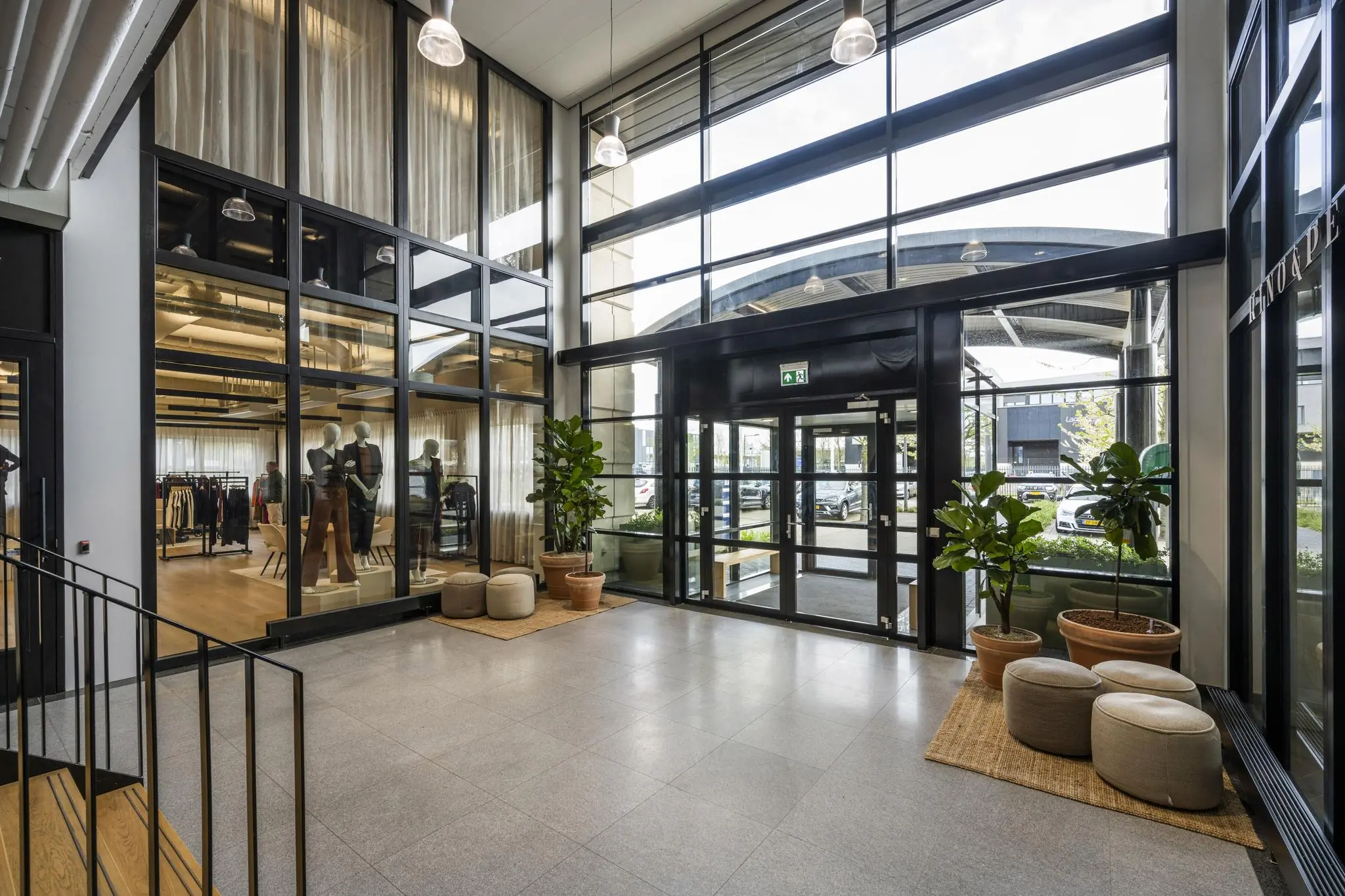 Ingang van een modern bedrijfsgebouw aan de Singaporestraat met glazen gevel, planten en zicht op een showroom met kleding.
