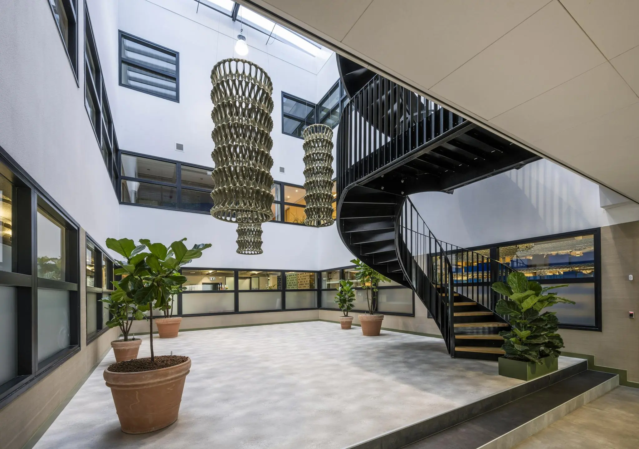 Moderne binnentuin in een kantoorpand aan de Singaporestraat met grote hanglampen, zwarte wenteltrap en planten in potten.