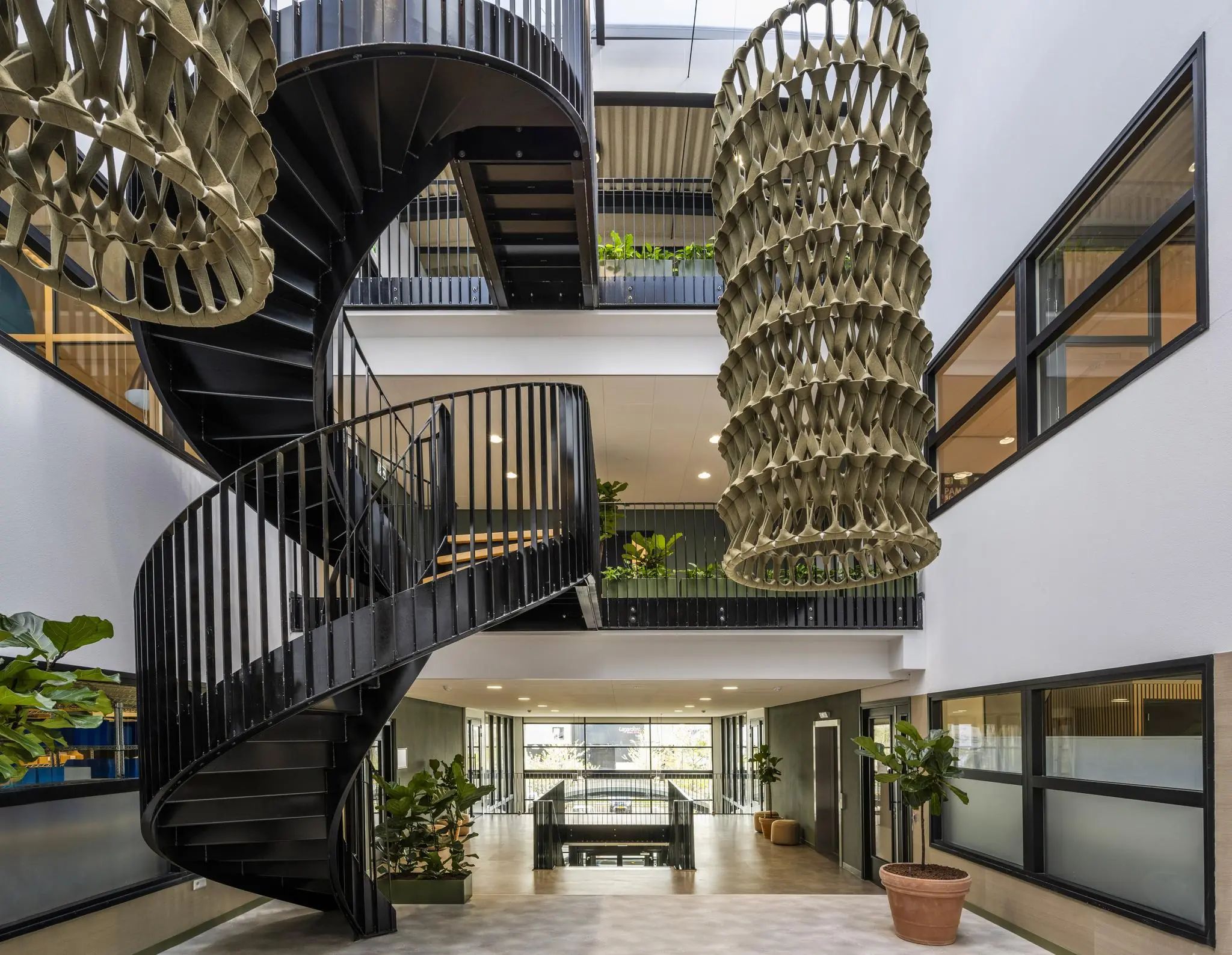 Moderne open kantoorruimte aan de Singaporestraat met een zwarte wenteltrap, hangende sculpturen en veel groen.