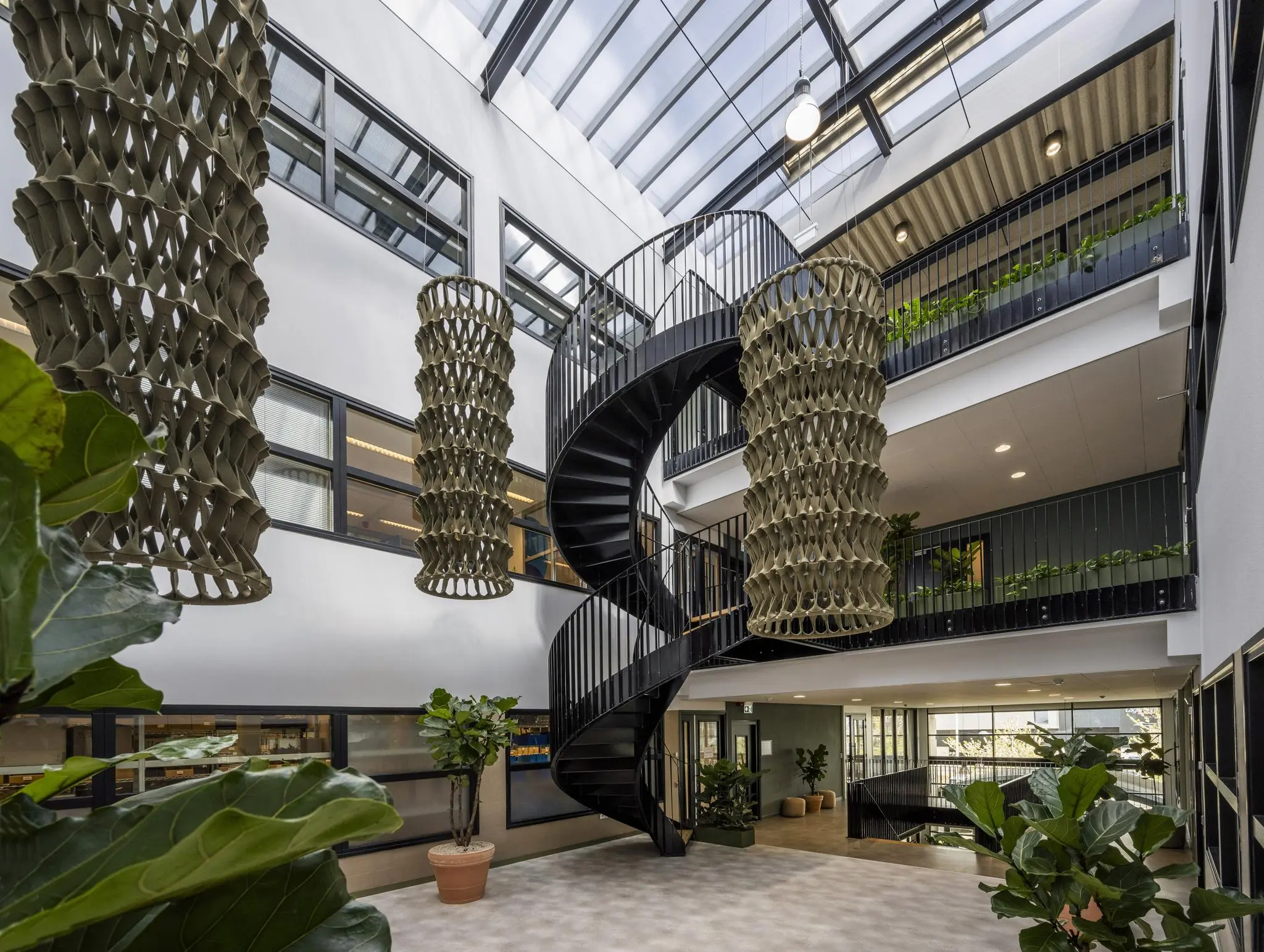 Moderne lichte atriumruimte aan de Singaporestraat met een zwarte wenteltrap, hangende kunstobjecten en veel groen.