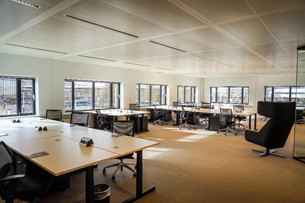 Ruim, modern kantoor met werkplekken en grote ramen aan het Prins Bernhardplein.
