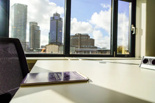 Kantoorruimte met uitzicht op het Prins Bernhardplein in Amsterdam, met een notitieboek op een bureau bij het raam.
