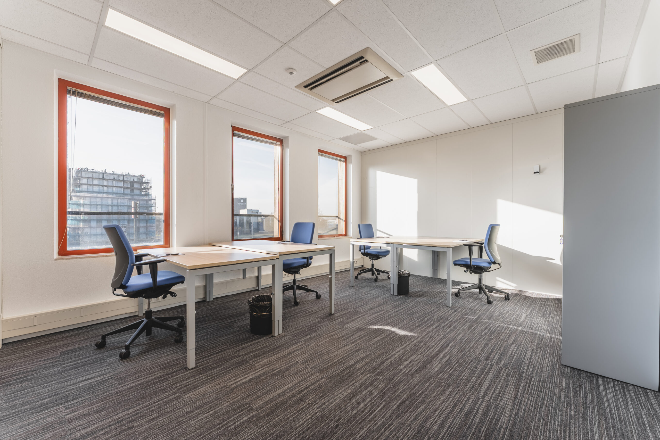 Een modern kantoor met drie werkplekken, voorzien van bureaus, stoelen en grote ramen.