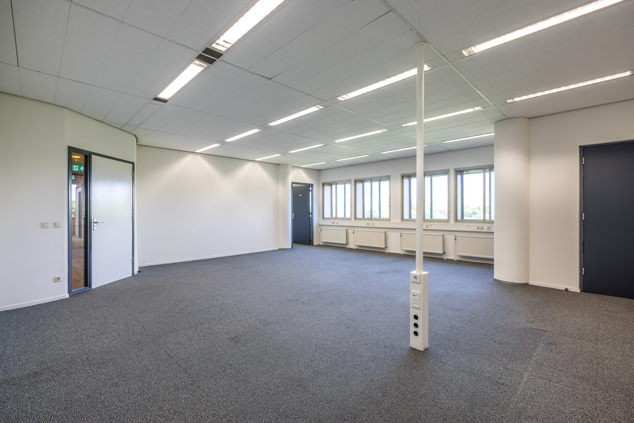 Een lege kantoorruimte met grijze vloerbedekking en meerdere ramen bij Element Offices in Utrecht.