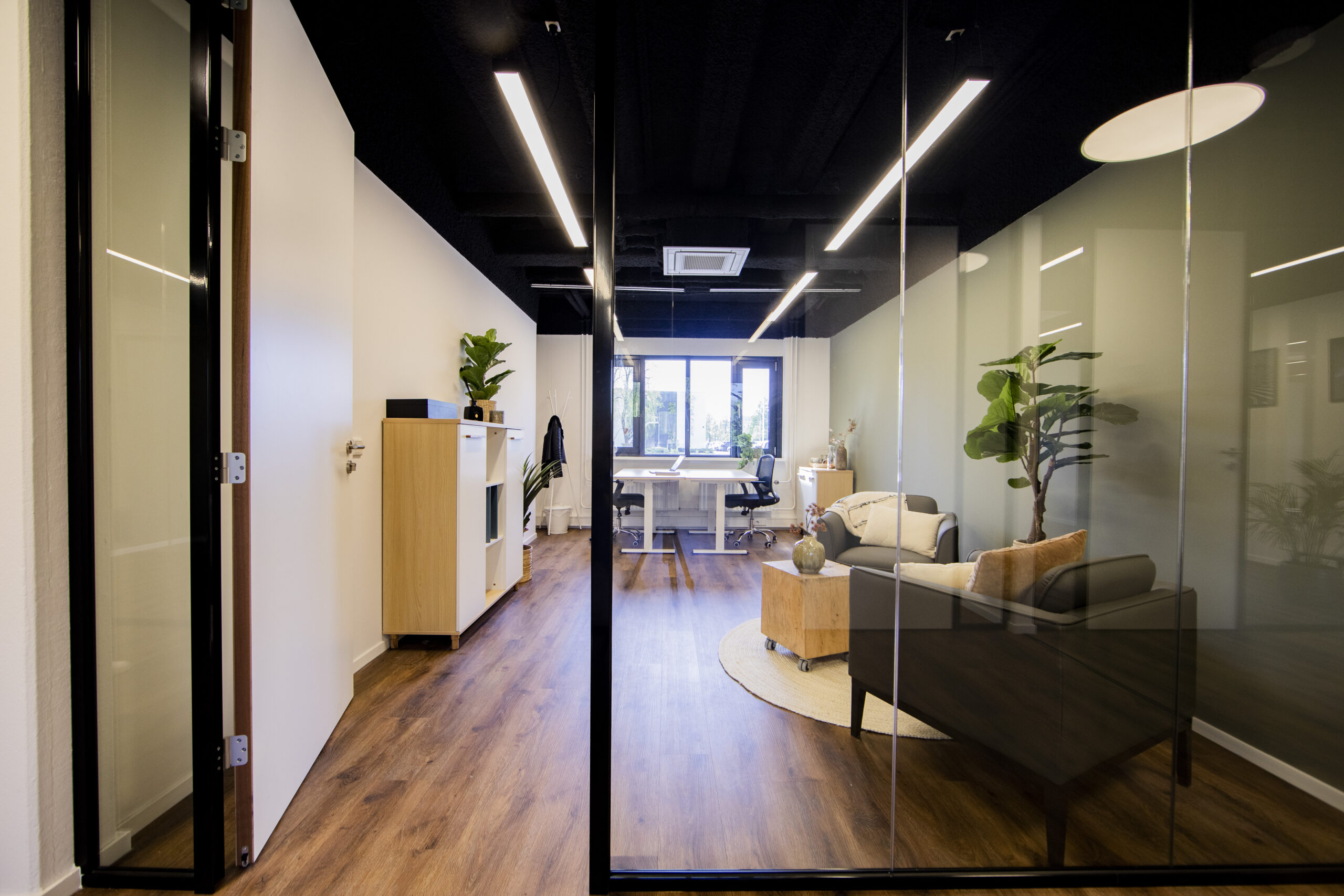 Een modern kantoor in Woerden met glazen wanden, houten vloer, en een uitnodigende loungehoek.