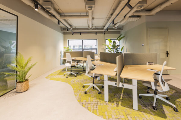 Een lichte, moderne kantoorruimte met bureaus, witte stoelen en groene planten.