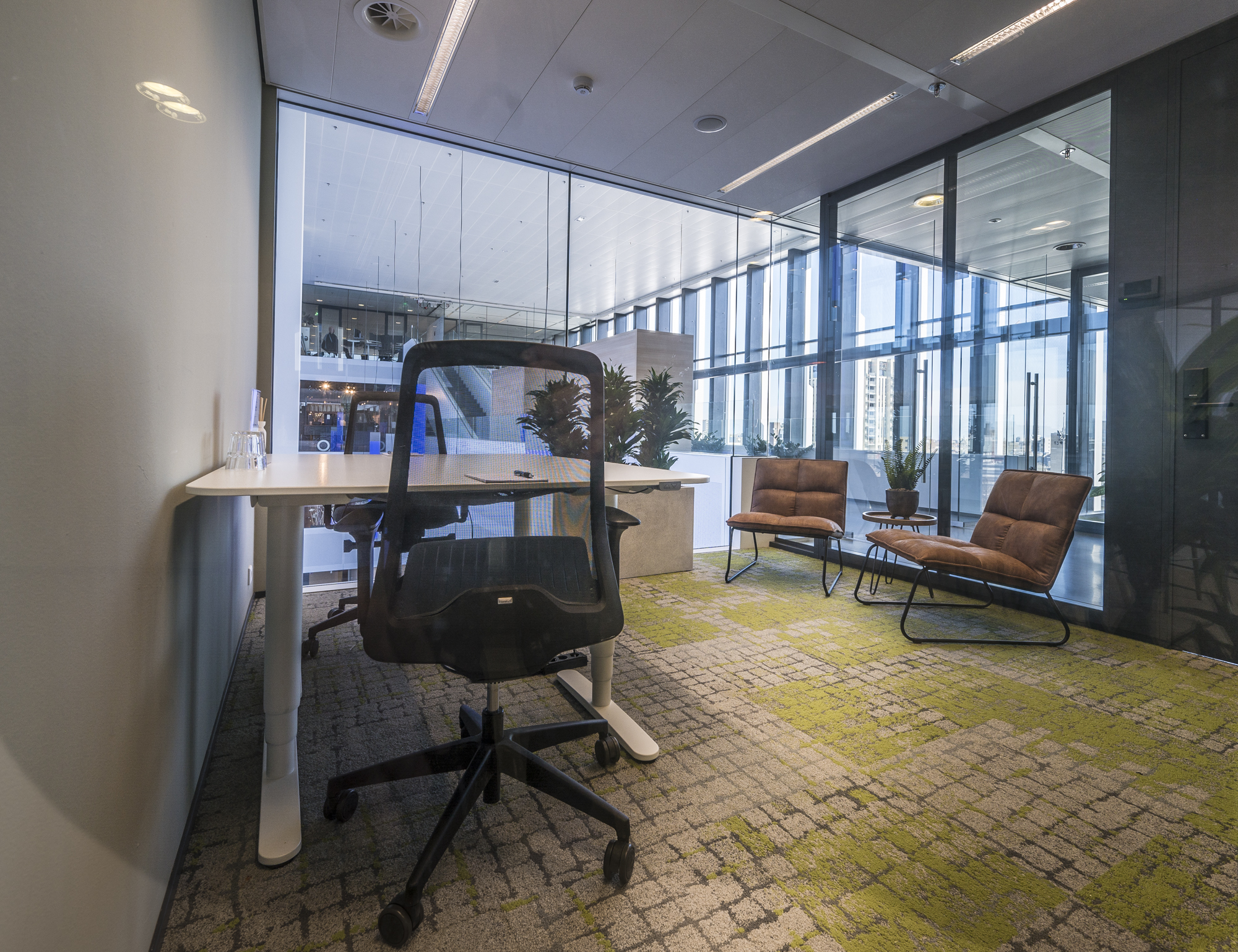 Een moderne kantoorruimte met glazen wanden, bureaustoel, bureau en twee bruine stoelen.