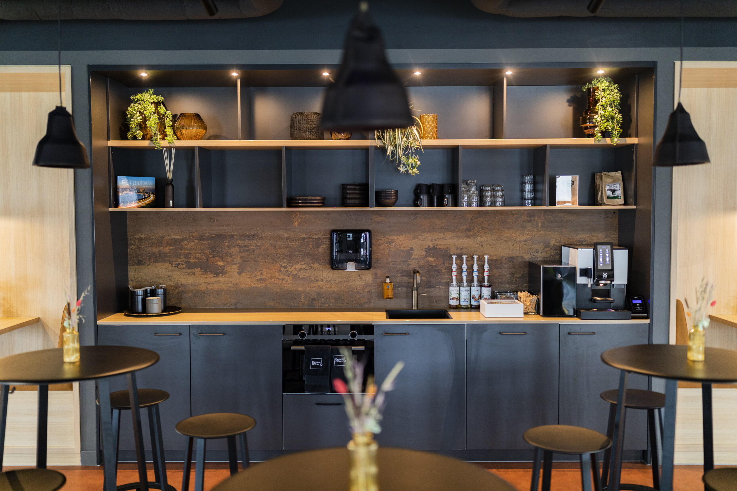 Een moderne kantoorkeuken met barkrukken, een koffiezetapparaat en open planken met decoraties.