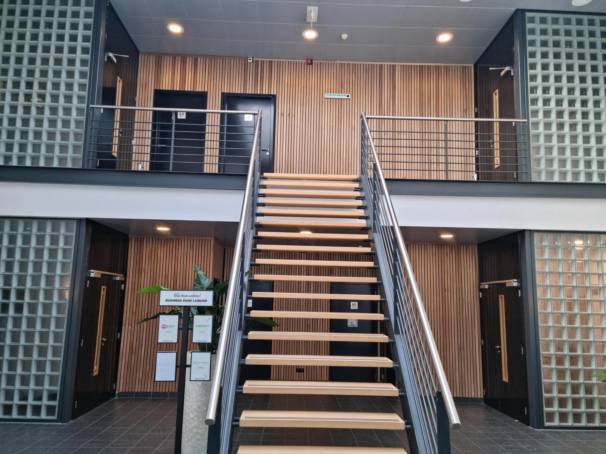 Moderne entreehal van Business Park Londen aan de Frankfurtstraat met een centrale houten trap en glazen bouwstenen.