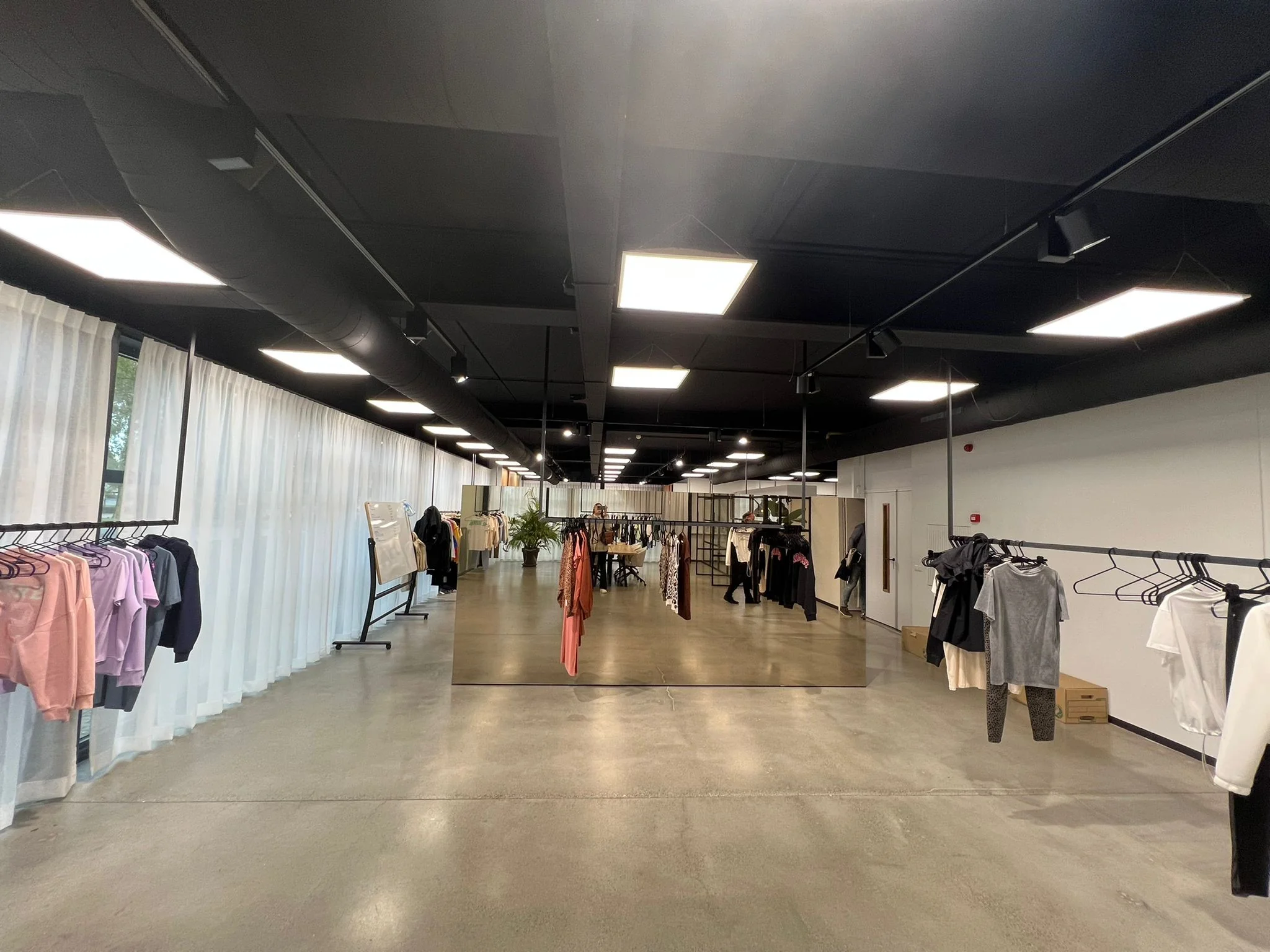 Ruime en moderne showroom aan de Frankfurtstraat met kledingrekken, spiegels en betonnen vloer.