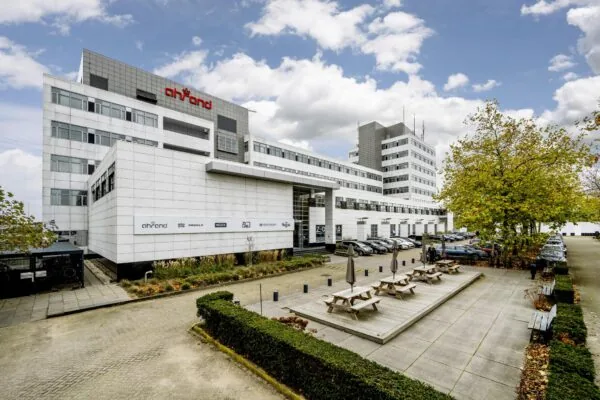 Modern kantoorgebouw aan de Laarderhoogtweg met Ahrend-logo, parkeerplaatsen en picknickbanken op een betegeld plein.