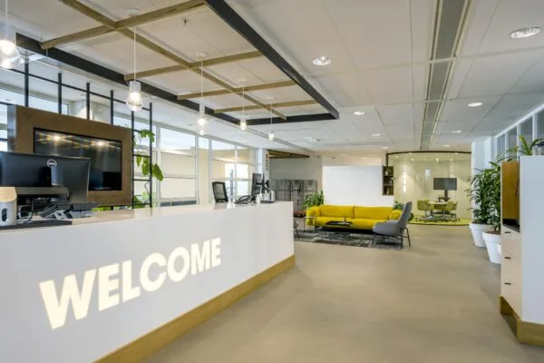 Moderne ontvangsthal aan de Laarderhoogtweg met een receptiebalie, gele zithoek en glazen vergaderruimte.