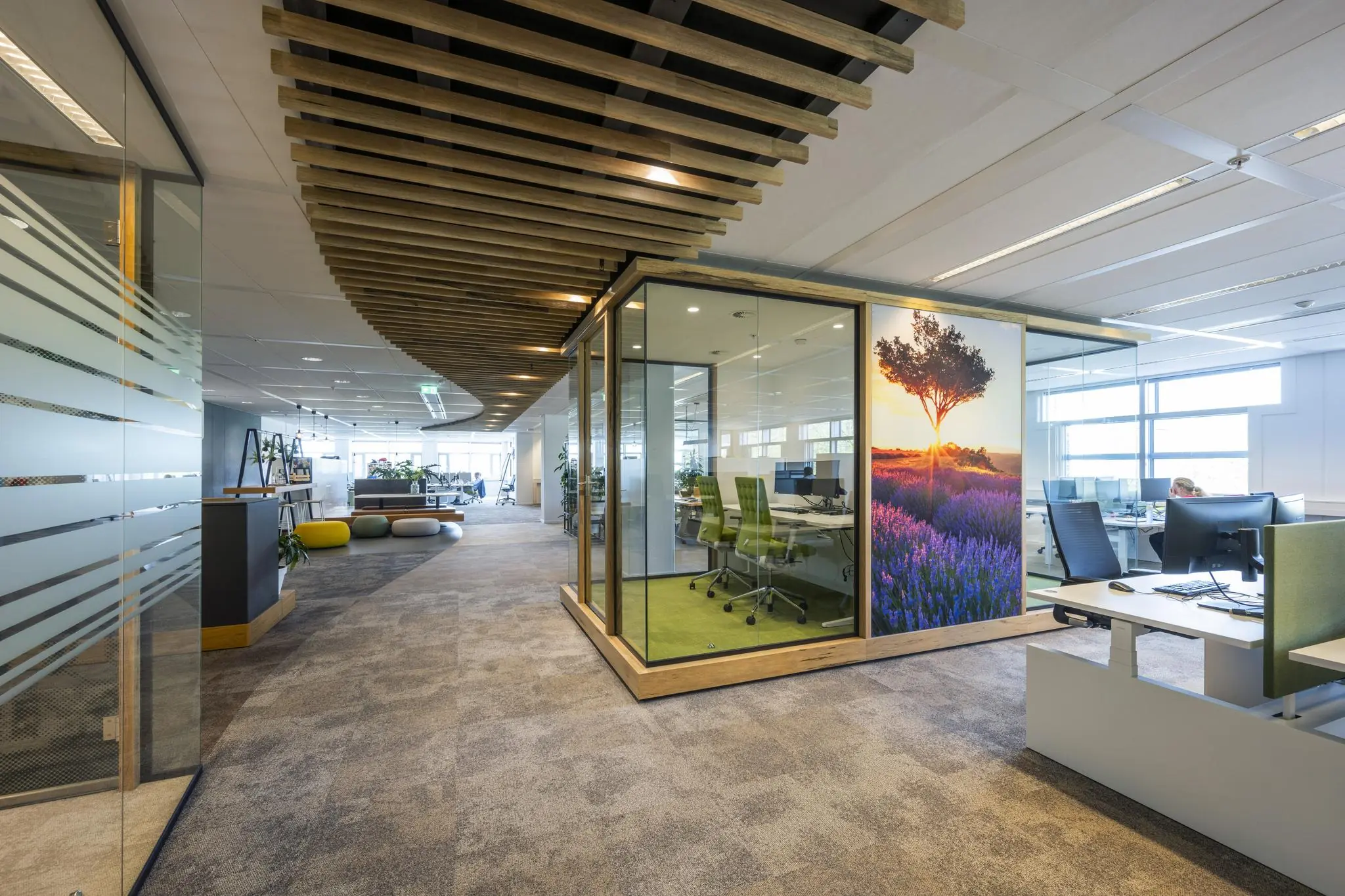 Moderne kantoorgang met glazen vergaderruimte, groene bureaustoelen en een wanddecoratie van een boom in een paarse bloemenweide.