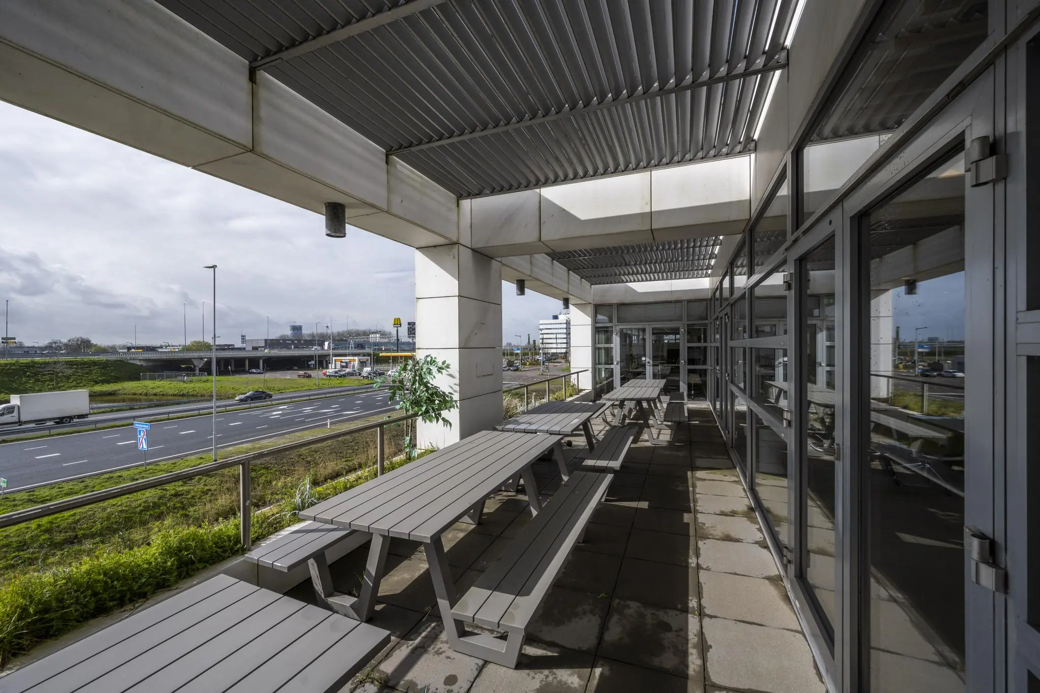 Overdekt terras met picknicktafels aan de Laarderhoogtweg met uitzicht op naastgelegen snelweg.