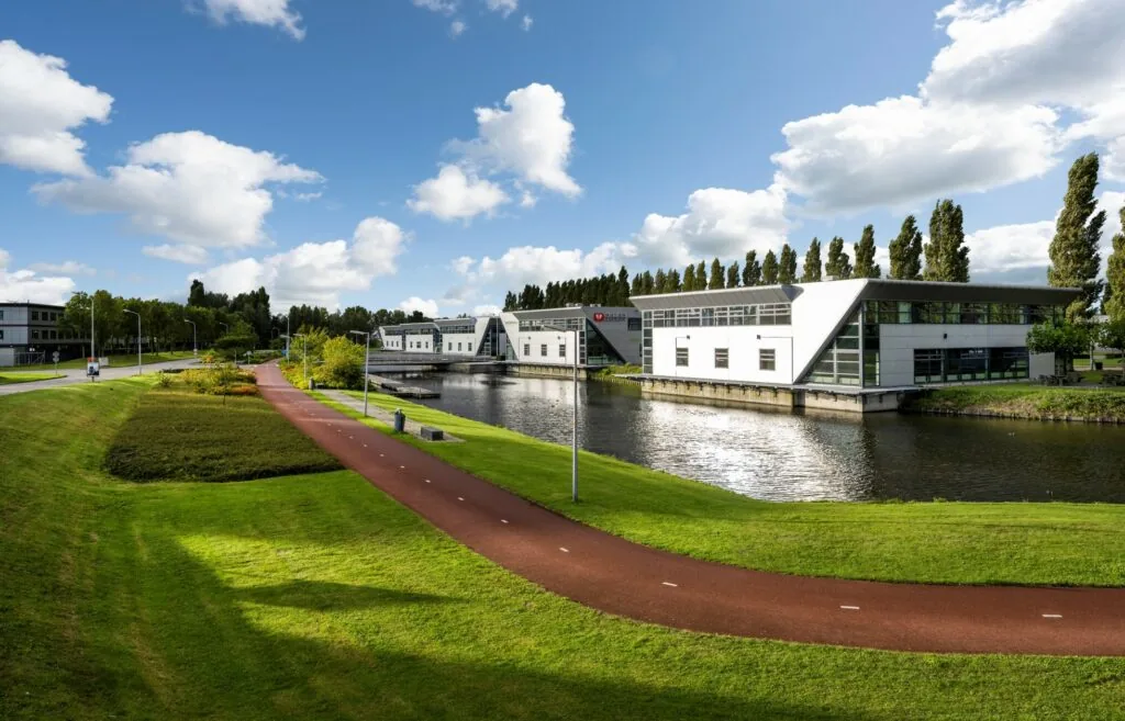 Modern kantoorgebouw aan het water aan de Frankfurtstraat in een groene, parkachtige omgeving met fietspad.