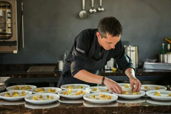 Chef-kok in zwarte outfit bereidt meerdere borden opmaak in een professionele keuken aan de Orteliuslaan.