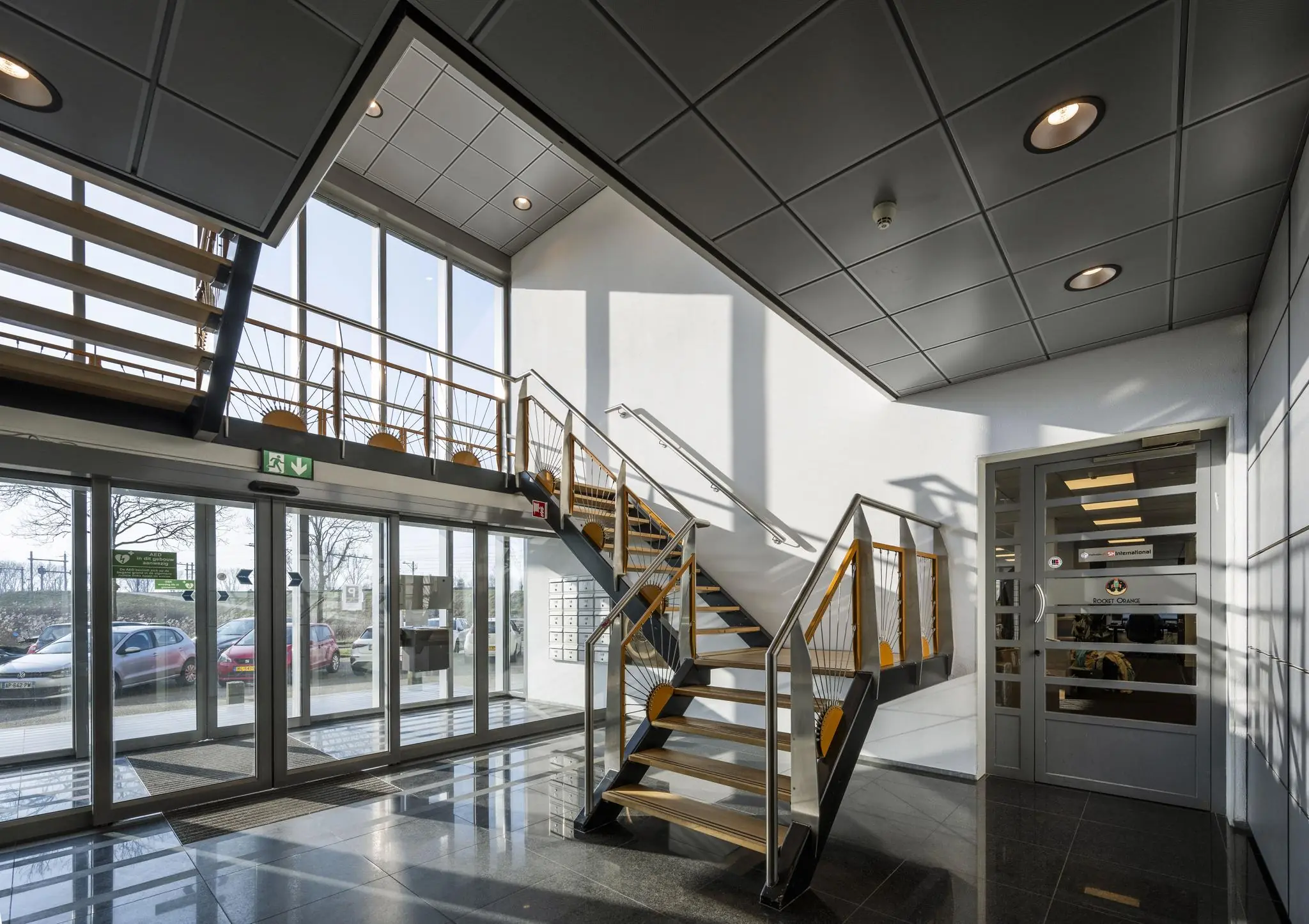 Moderne entreehal aan de Joan Muyskenweg met glazen schuifdeuren, trap met houten leuningen en veel daglicht.