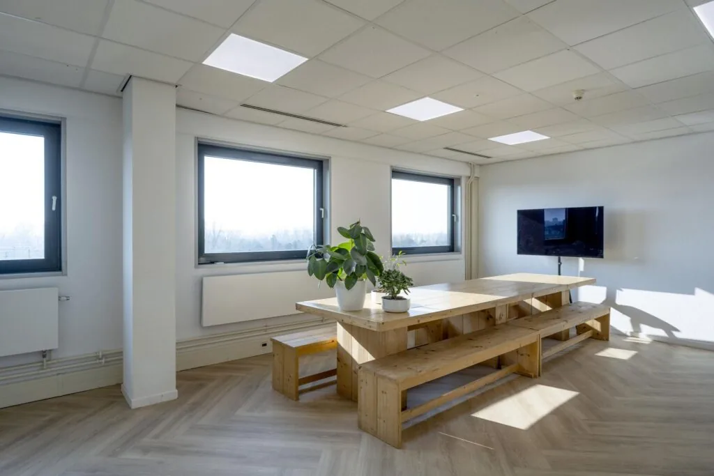 Moderne vergaderruimte aan de Joan Muyskenweg met houten tafel, planten, wand-tv en grote ramen met uitzicht.