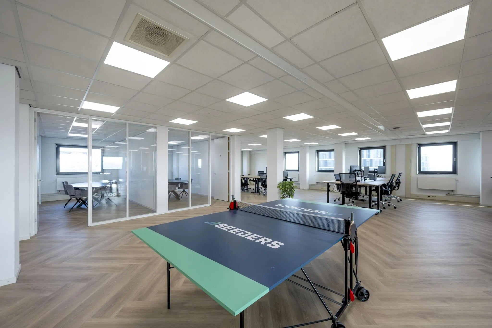 Modern kantoorinterieur aan de Joan Muyskenweg met glazen vergaderruimtes, bureaus en een tafeltennistafel van Seeders.