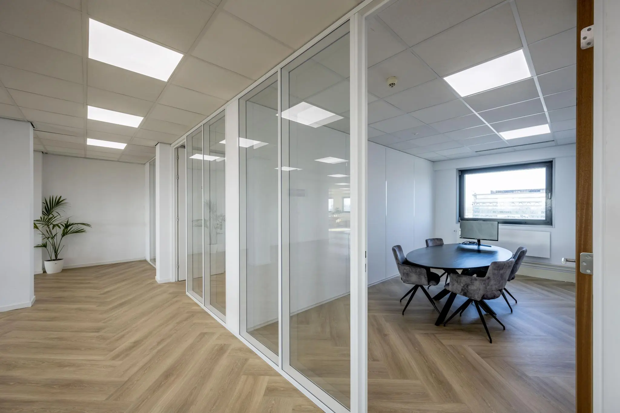 Modern kantoorinterieur aan de Joan Muyskenweg met glazen vergaderruimtes en houtlook visgraatvloer.