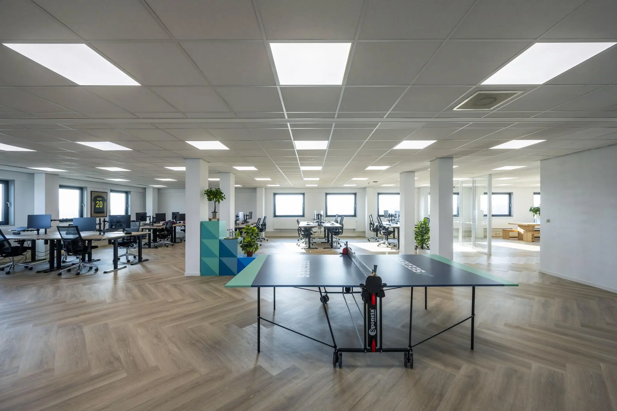 Moderne open kantoorruimte aan de Joan Muyskenweg met bureaus, een pingpongtafel en planten.