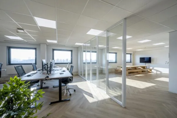 Modern en licht kantoorinterieur aan de Joan Muyskenweg met werkplekken en glazen vergaderruimte.