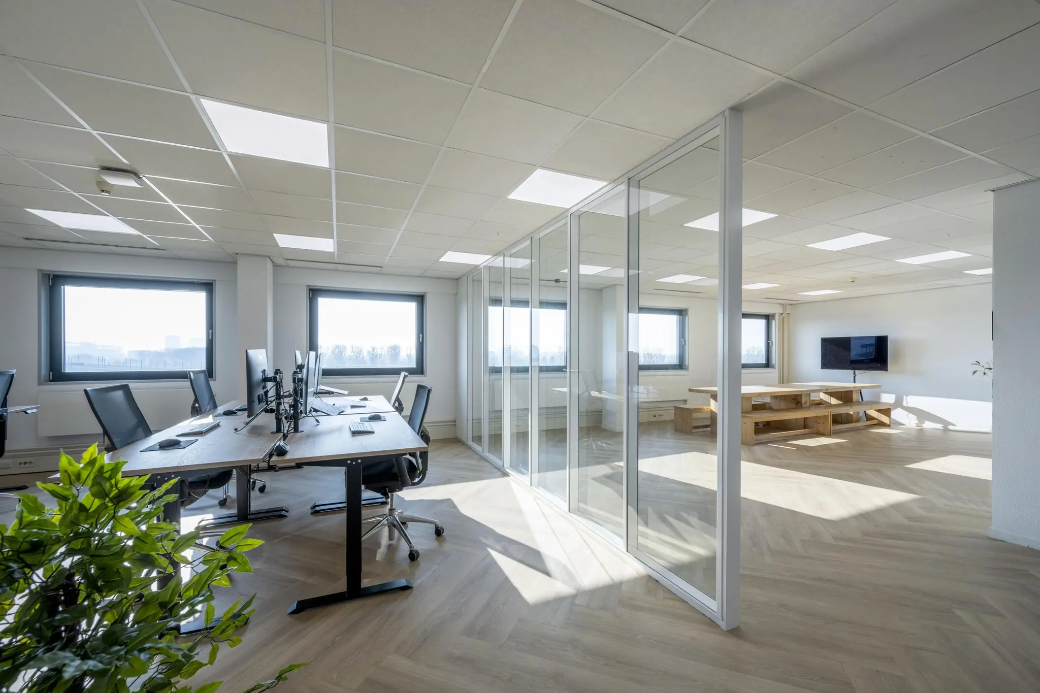 Modern en licht kantoorinterieur aan de Joan Muyskenweg met werkplekken en glazen vergaderruimte.