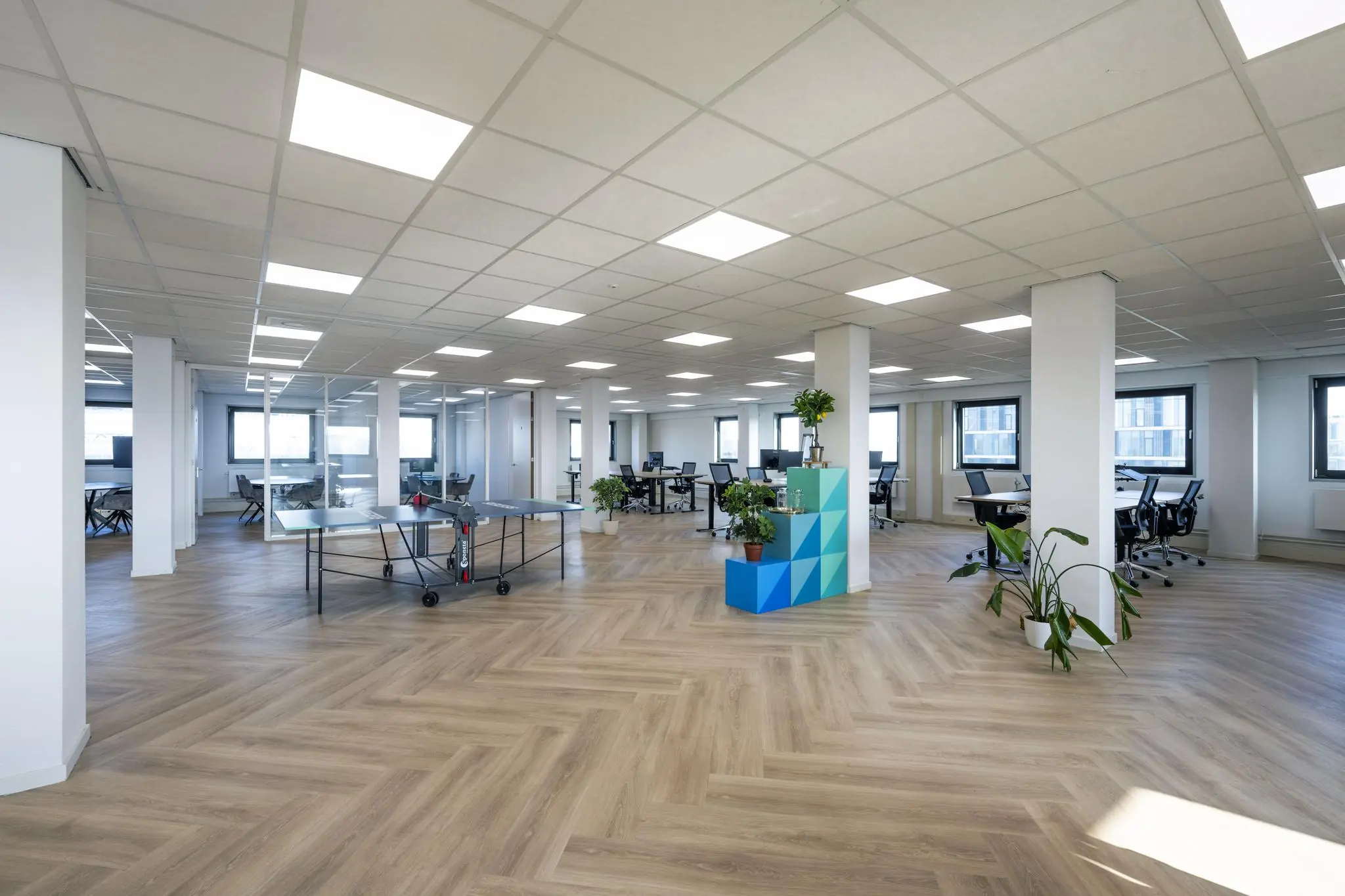 Moderne, open kantoorruimte aan de Joan Muyskenweg met werkplekken, planten, een tafeltennistafel en veel natuurlijk licht.